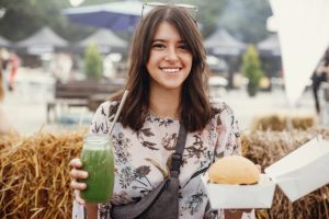 Smiling woman holding healthy drink and sandwich at a Missoula Farmers Market